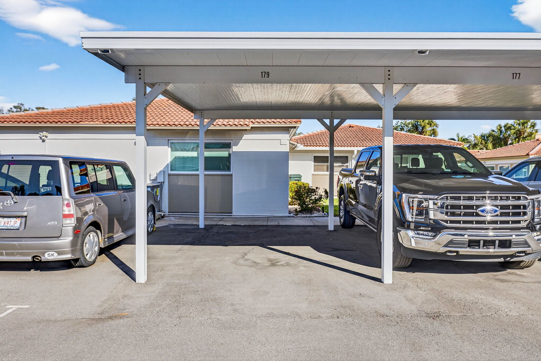 A covered parking area with two vehicles, a minivan and a pickup truck, parked under a white canopy.