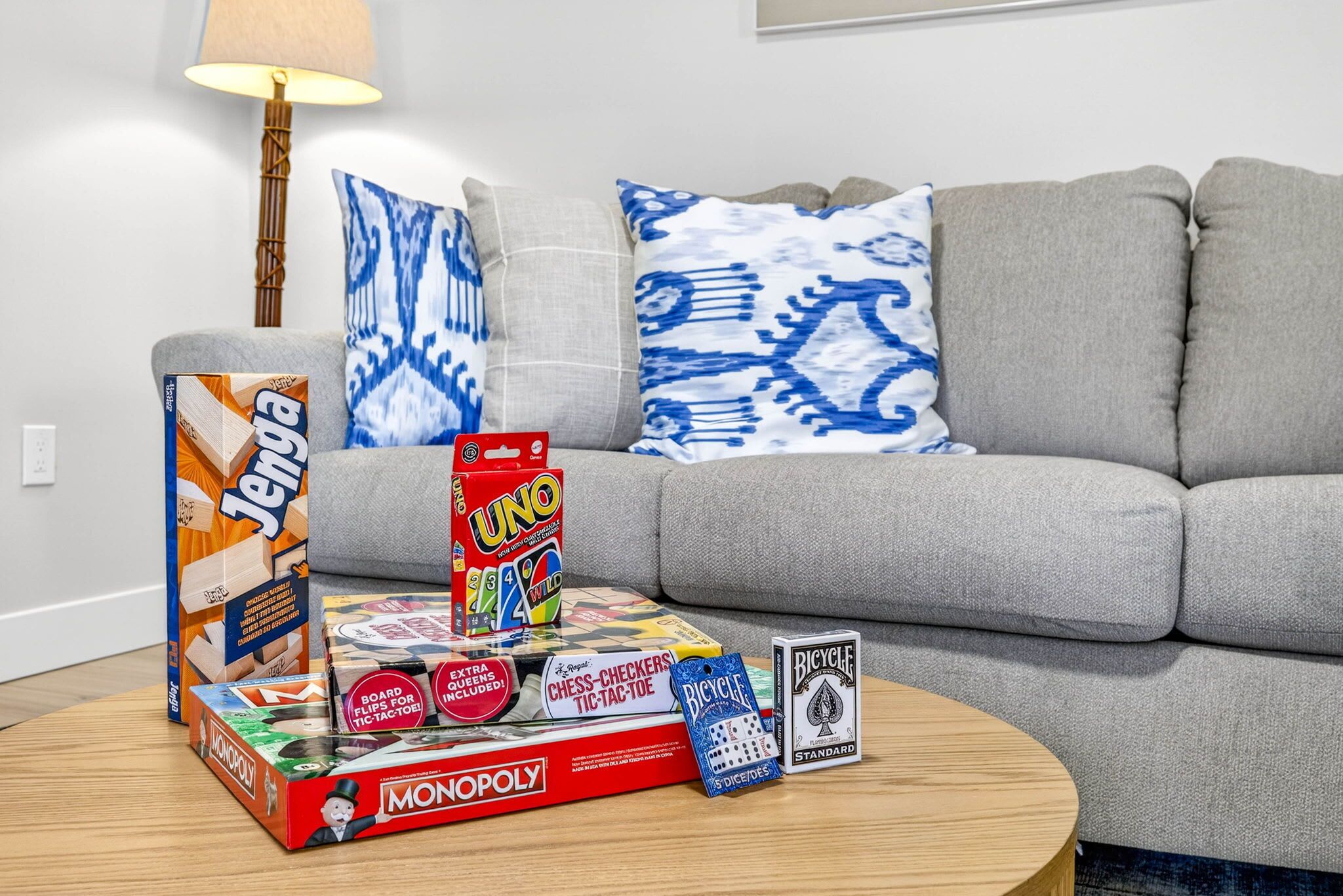 A living room with a grey sofa, a wooden coffee table, and various board games including Monopoly, Jenga, UNO, and Bicycle.