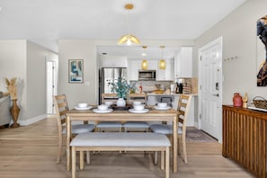 A dining area with a wooden table set for six, a bench, and a kitchen in the background with white cabinets and a microwave. - Salt & Sol - Your Siesta Key retreat for 6 (Sarasota)
