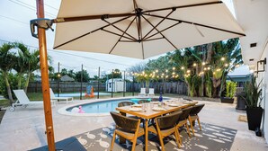 Patio esterno con piscina, tavolo da pranzo, sedie e ombrellone.