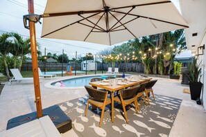 Eine Außenpatio mit Pool, Esstisch, Stühlen und Sonnenschirm.