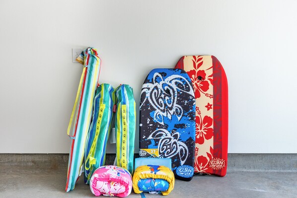 Una colección de bolsos coloridos y una tabla de surf frente a un fondo liso.