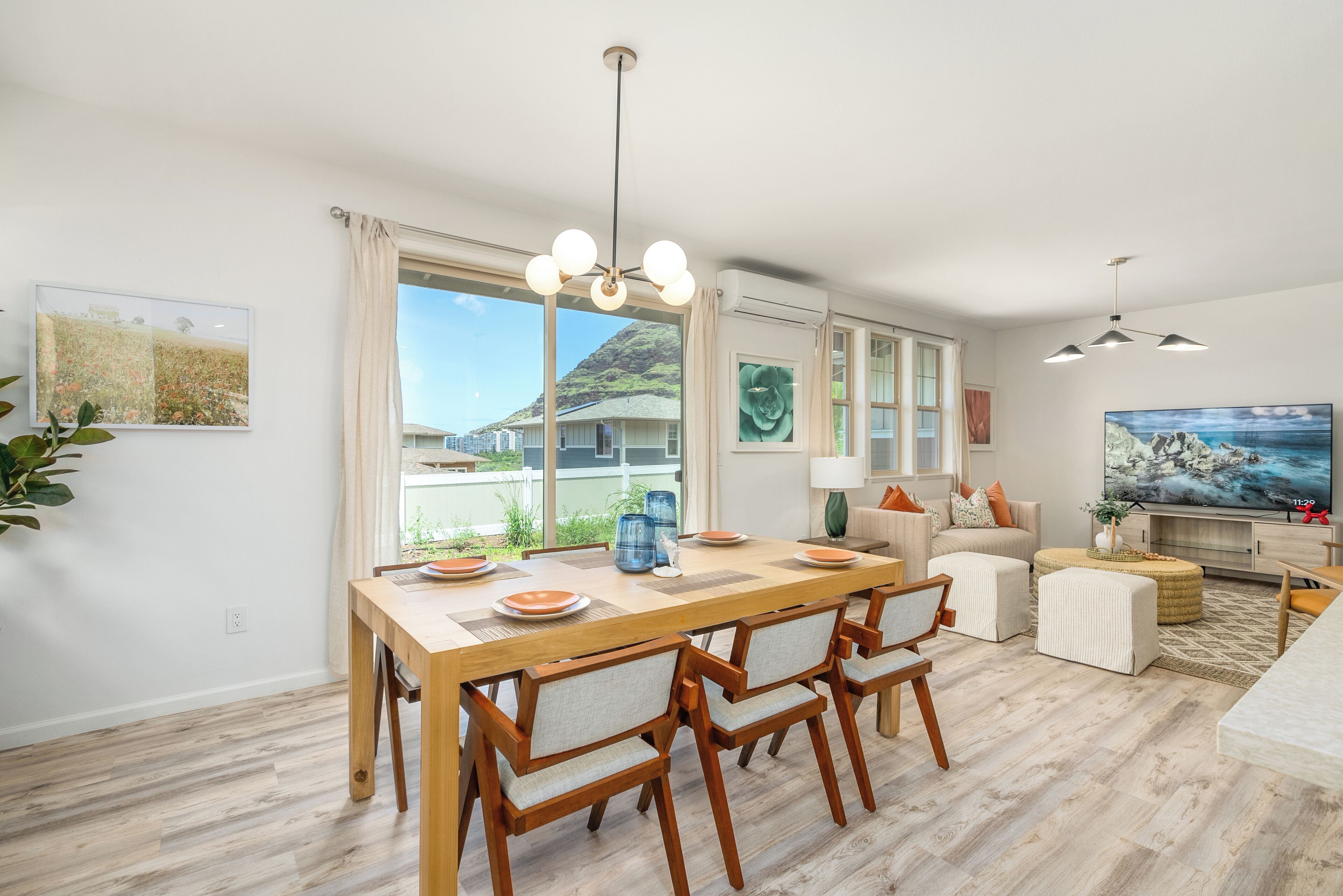 A modern living room with a dining area, large windows, and a view of a mountain.