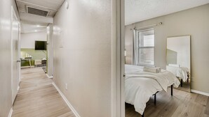 A hotel room with a large bed, a bedside table, a mirror, and a window with blinds. - Urban Chic Getaway 2B | Sleeps 6 | Pool, Prkg, W/D (Austin)