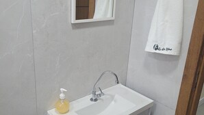 A bathroom with a white sink, a mirror, and a towel rack. - Furnished one-bedroom apartment in Balneário Gaivota, right in the center. (Balneário Gaivota)