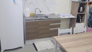 A compact kitchen with a refrigerator, sink, wooden cabinets, and a microwave. - Furnished one-bedroom apartment in Balneário Gaivota, right in the center. (Balneário Gaivota)