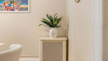 A room with a white radiator, a potted plant, and a framed cityscape painting on the wall.