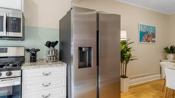 A kitchen with a stainless steel refrigerator, a microwave, a stove, and a sink. There is a plant and a painting on the wall.