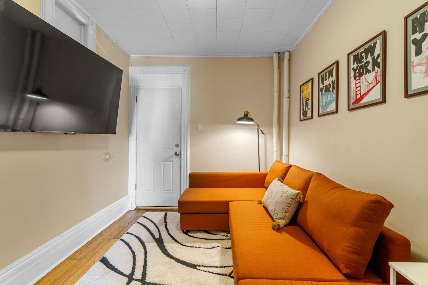 A living room with a sectional sofa, a flat-screen TV mounted on the wall, a door, and framed pictures on the wall.