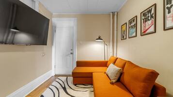 A living room with a sectional sofa, a flat-screen TV mounted on the wall, a door, and framed pictures on the wall.