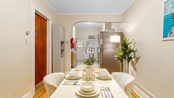 Un comedor con una mesa preparada para cuatro personas, un refrigerador y una planta.