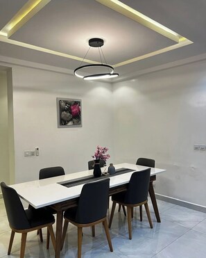 A modern dining area with a white table, black chairs, and a pendant light. - Malikis Court (Abuja)