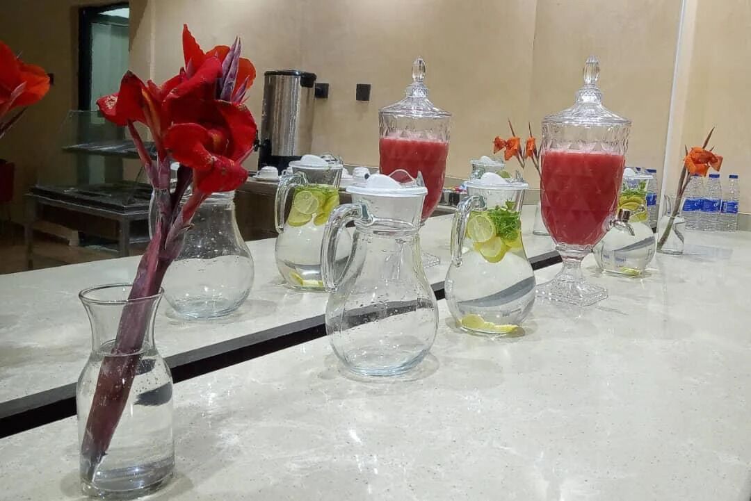 A bar area with various glass containers holding drinks, some with lime slices, and a vase with red flowers.