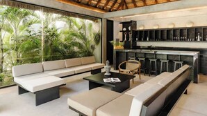 Un espace de vie moderne doté d’une grande fenêtre donnant sur une végétation luxuriante, d’un coin salon et d’un bar avec des étagères.