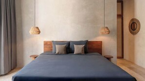 Une chambre moderne avec une tête de lit en bois, un grand lit recouvert d’une couverture bleu foncé, deux tables de chevet et deux lampes suspendues.