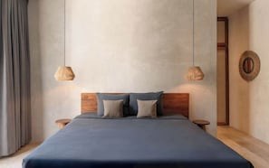 Ein modernes Schlafzimmer mit einem hölzernen Kopfteil, einem großen Bett mit dunkelblauer Bettdecke, zwei Nachttischen und zwei Pendelleuchten.