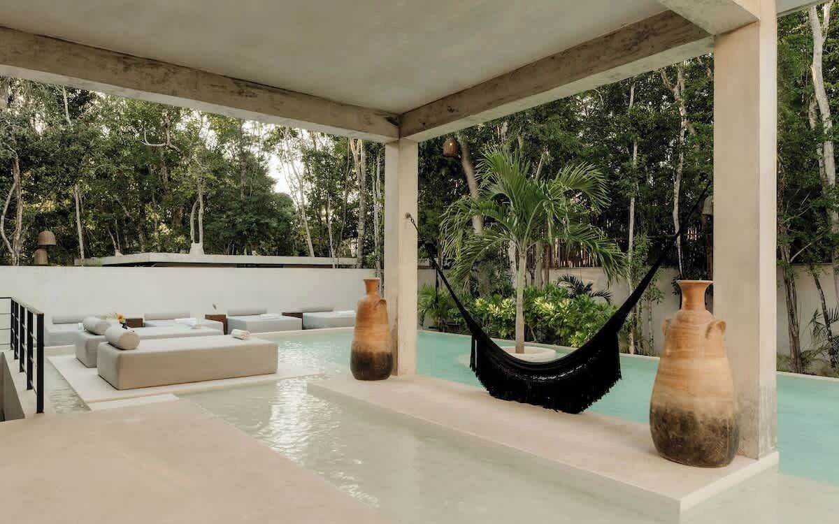 A pool area with a hammock, seating, and large vases.