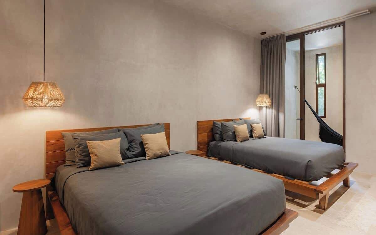 A bedroom with two beds, a wooden headboard, a hanging light fixture, and a view of a staircase.