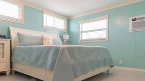A bedroom with a bed, a nightstand, a lamp, and a wall-mounted air conditioner. - Flamingo Inn - Standard King with Kitchenette (Fort Myers Beach)