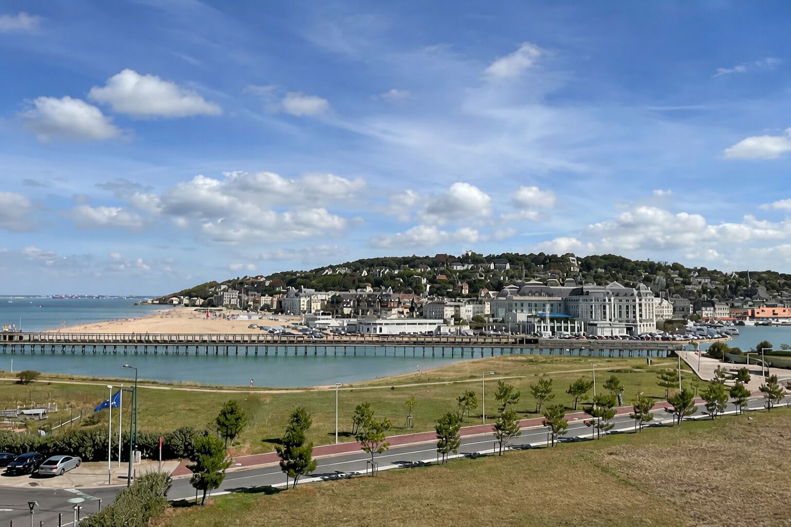 A coastal town with a beach, a pier, and a hill with buildings.