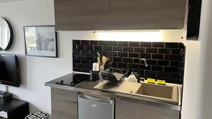 A modern kitchen with a black tiled backsplash, a stainless steel sink, and a compact dishwasher. - ✨ Sea View Studio with Balcony – Deauville Boardwalk ✨ (Deauville)