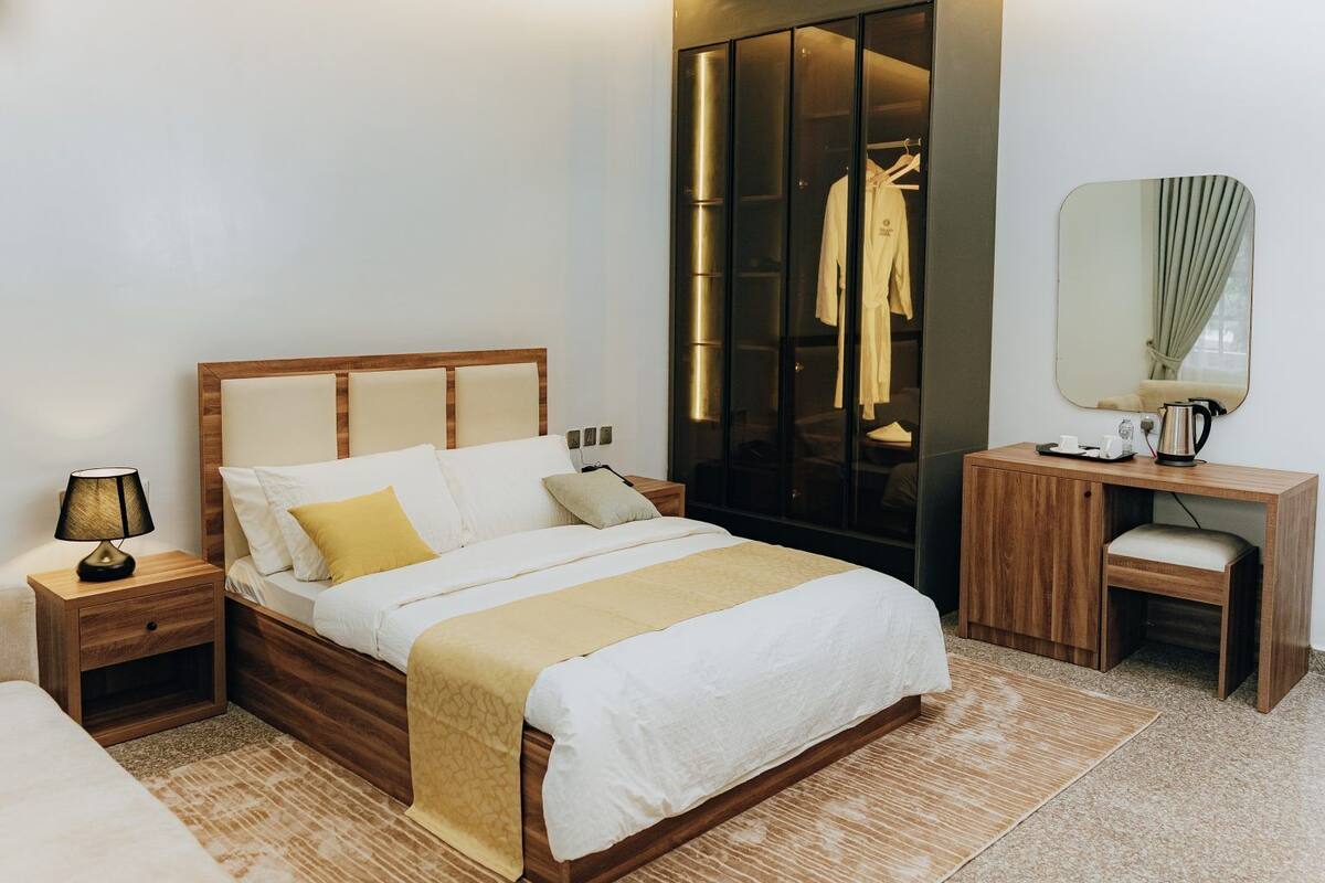 Una habitación de hotel con cama, mesitas de noche, escritorio, espejo y armario.