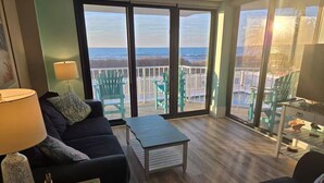 Un salón amplio con un gran ventanal corredera que da a un balcón con vistas a la playa.