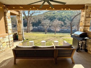 Eine überdachte Terrasse mit einer Steinmauer, einer Holzbank, einem Grill und Blick auf eine bewaldete Landschaft.