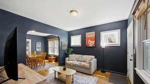 Ein Wohnzimmer mit Fernseher, Esstisch aus Holz und einer Couch.