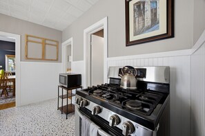A kitchen with a stove, a television on a stand, and a framed picture on the wall. - Charming Tremont 3BR - Minutes to Downtown (Cleveland)