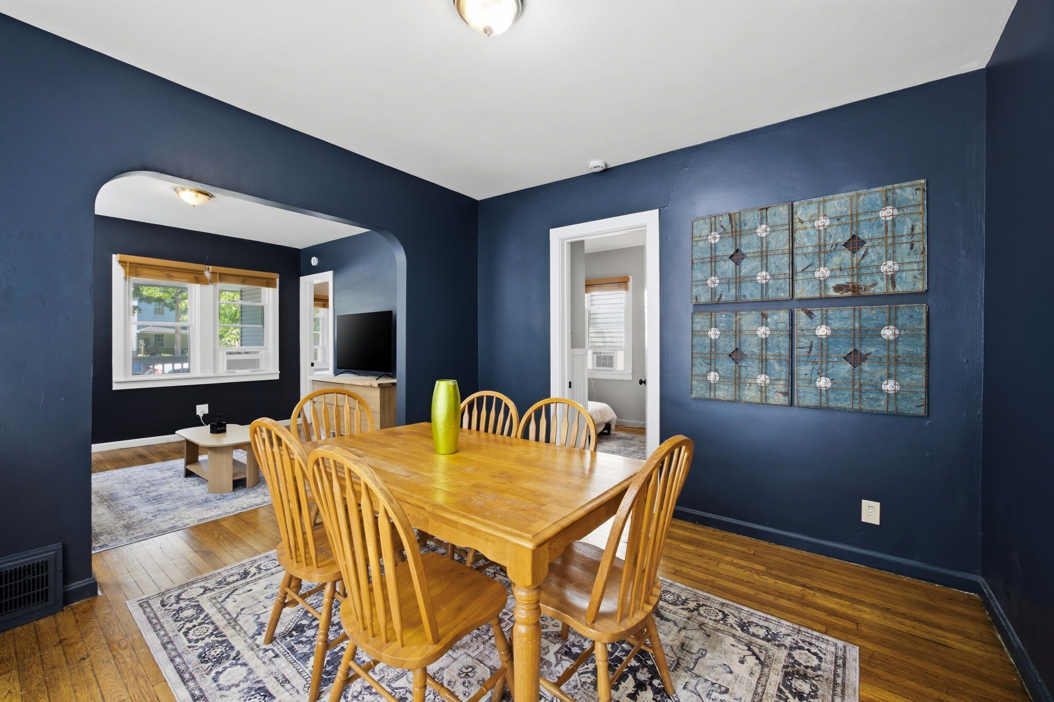 A dining room with a wooden table and chairs, a vase, and a blue wall with decorative tiles.
