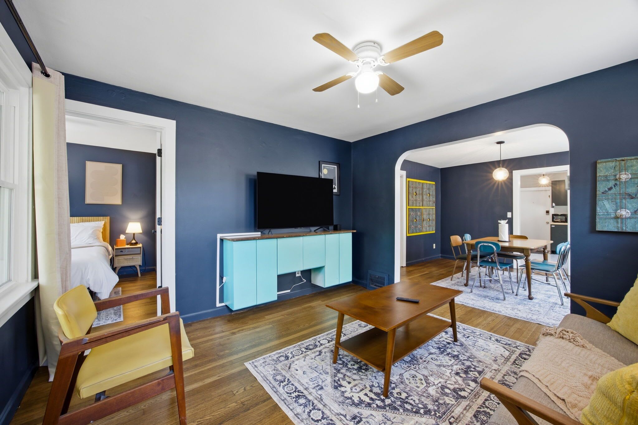 A living room with a TV, wooden furniture, a ceiling fan, and a dining area with chairs and a table.