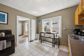 A kitchen with a stove, sink, and window. There is a dining table with chairs. - Bright Tremont 2BR - Near Downtown CLE & Clinic (Cleveland)