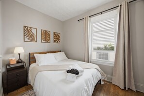 A neatly made bed with white linens, a bedside table with a lamp and tissues, and a window with curtains. - Bright Tremont 2BR - Near Downtown CLE & Clinic (Cleveland)