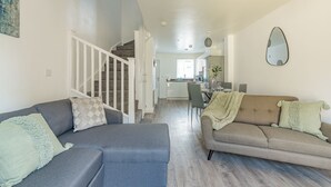 Een ruime woonkamer met een trap, een eettafel met stoelen en een bank.