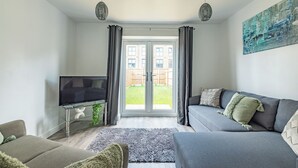 Een moderne woonkamer met een grijze bank, een flatscreen televisie en een glazen salontafel.