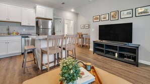 A modern kitchen with white cabinets, stainless steel appliances, and a dining area with wooden chairs and a table. - Downtown Condo | 10 Min to FSU Stadium & Campus (Tallahassee)
