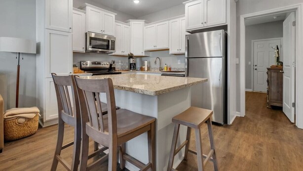 A modern kitchen with white cabinets, stainless steel appliances, and a central island with bar stools. - Downtown Condo | 10 Min to FSU Stadium & Campus (Tallahassee)