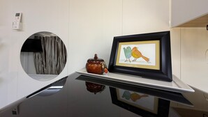 Une cuisine moderne avec un plan de travail noir, une œuvre d’art encadrée représentant deux oiseaux, un pot en céramique et un miroir rond accroché au mur.