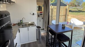Une cuisine compacte dotée d’appareils électroménagers modernes, un coin repas avec une table et des chaises, et une grande porte-fenêtre coulissante donnant sur une terrasse extérieure.