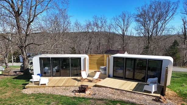 Une maison mobile moderne et compacte, dotée de grandes fenêtres, d’une terrasse en bois et d’un espace salon extérieur.