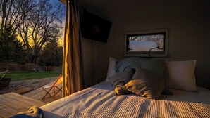 Une chambre à coucher avec un lit, un téléviseur fixé au mur et une fenêtre donnant sur un jardin.