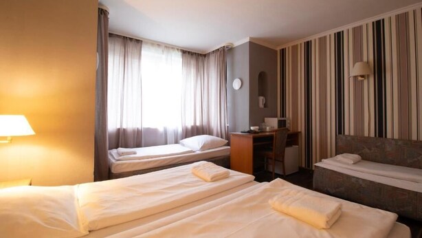Une chambre d’hôtel avec deux lits simples, un bureau, une chaise, un canapé, une lampe et une fenêtre avec des rideaux.