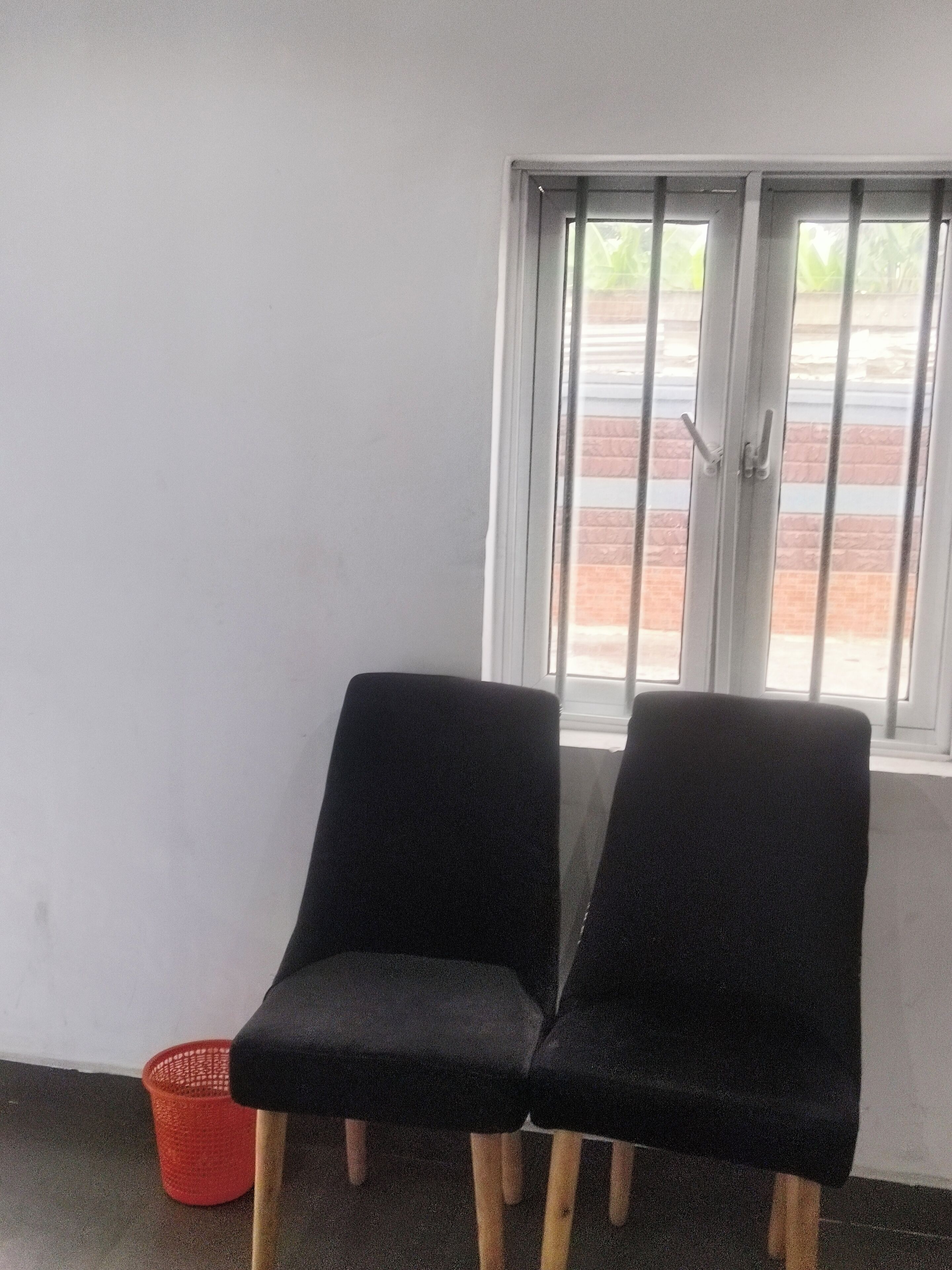 Two black chairs with wooden legs in a room with a window and a red basket on the floor.