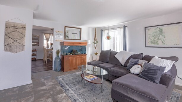 Un salon moderne avec un canapé gris, une table basse en verre et un vase bleu. On aperçoit, au fond, un meuble en bois et un aquarium.