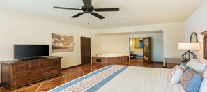 Ein Hotelzimmer mit Bett, Fernseher, Deckenventilator, Badezimmer mit Badewanne und einem zur anderen Kammer führenden Flur.