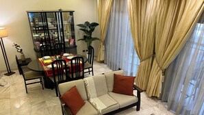 Uma sala de estar com sofá, mesa de jantar, cadeiras, um armário de vidro e uma janela grande com cortinas.