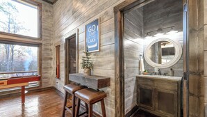 A rustic bathroom with wooden walls, a wooden bench, a sign that says "GO JUMP IN THE LAKE", and a round mirror. - Luxury Farmhouse Cabin-3 King Suites + Bunk/Game (Broken Bow)