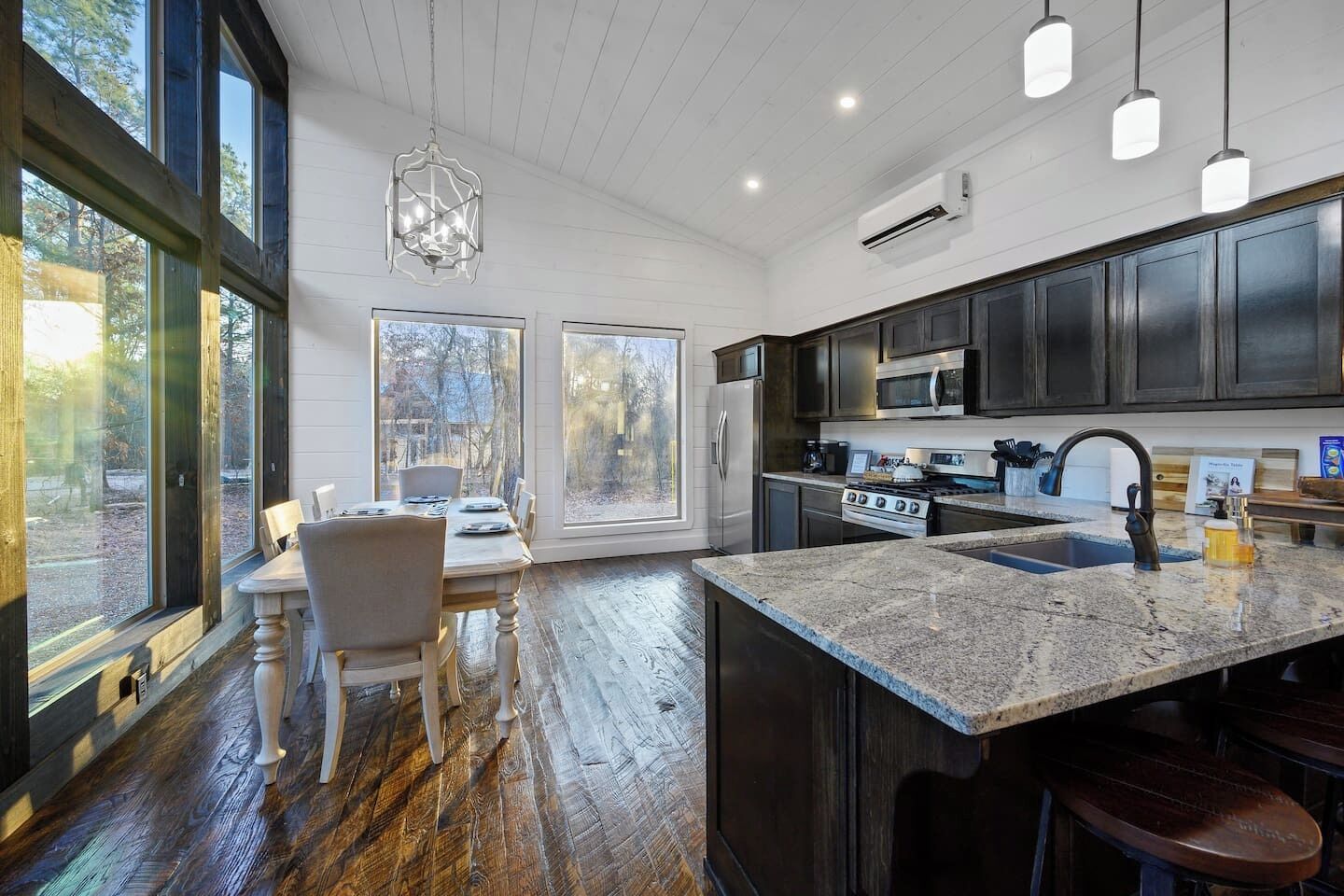 A modern kitchen with dark wood cabinets, a granite island, and a large window overlooking a wooded area.