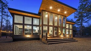 A modern cabin with large glass windows, a wooden exterior, and a gravel driveway. - Luxury Farmhouse Cabin-3 King Suites + Bunk/Game (Broken Bow)